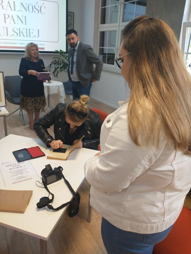 Na zdjęciu sygnowanie książki pieczęcią Narodowego Czytania, w tle uczestnicy spotkania 