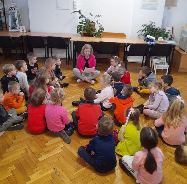 Dzieci siedzą w kręgu i słuchają prowadzącej