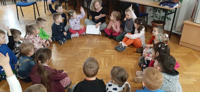 Dzieci siedzą w kręgu i słuchają prowadzącej