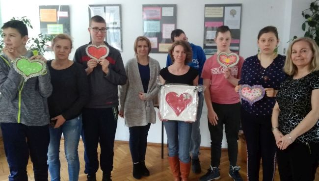 Wszyscy uczniowie wraz z nauczycielami  pozują do zdjęcia, trzymając w rękach ozdabiane przez siebie papierowe serca.