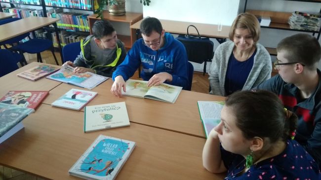 Uczniowie siedzą przy stole i oglądają książki dla dzieci o miłośći i przyjażni.