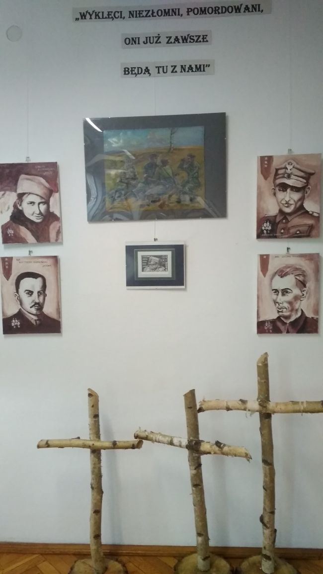 W górnej części zdjęcia tytuł wystawy, w części centralnej portrety przedstawiające sylwetki Żołnierzy Wyklętych, na dole trzy drewniane krzyże