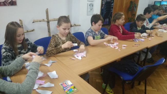 Uczniowie siedzą w ławkach i rwą na drobne kawałki pokolorowane wcześniej kartki papieru.