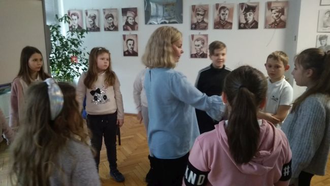 Uczniowie stoją w kręgu i uczestniczą w zabawie ruchowej, którą prowadzi nauczyciel bibliotekarz.