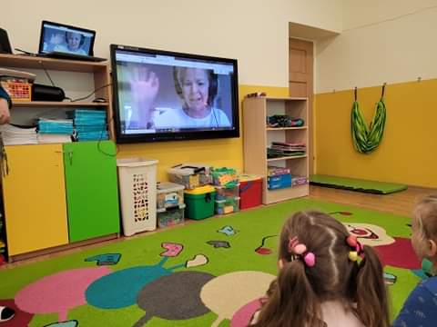Przedszkolaki siedza na dywanie i oglądają na duzym ekranie telewizora prowadząc ą zajęcia