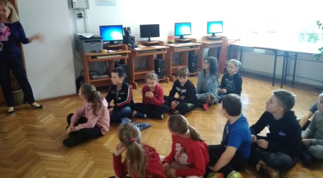 Kolejni uczniowie siedzą na podłodze po turecku, w dwóch rzędach 