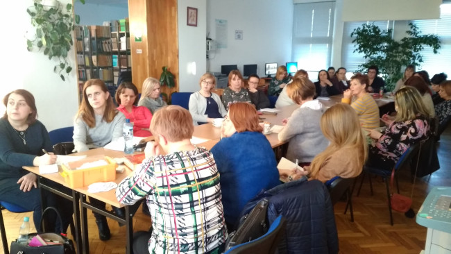 Nauczyciele poloniści siedzą przy stolikach i słuchają wykładu 