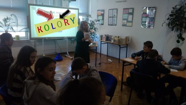 Na środku sali stoi prowadząca z wydrukowanym labiryntem i tłumaczy wykonanie zadania. Za nią znajduje się tablica interaktywna, na krórej widnieje napis 