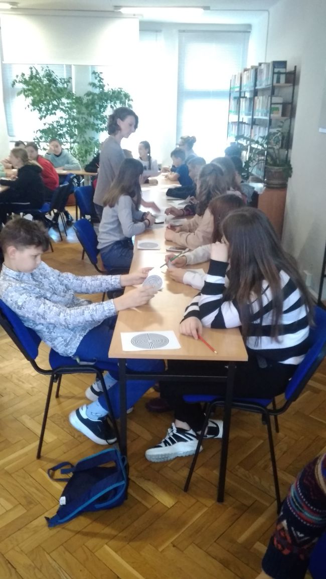 Uczniowie siedzą w ławkach i rozwiązują na kartkach labirynt.