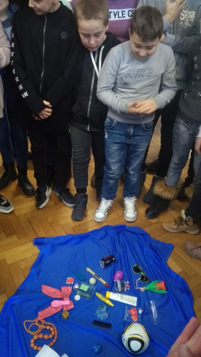 Zbliżenie na dwóch uczniów, którzy obserwują drobne przedmioty rozłożone na podłodze, na niebieskiej chuście.