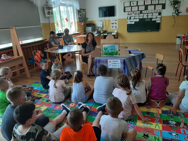 Uczniowie siedząc na dywanie słuchają bajki przedstawionej w teatrzyku Kamishibai.