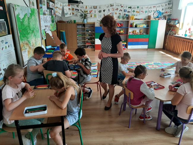 Uczniowie przy stolikach wykonują prace plastyczne.