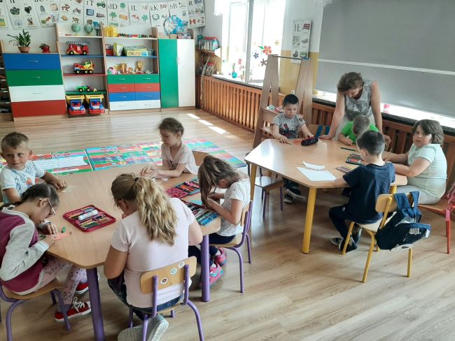 Uczniowie przy stolikach wykonują prace plastyczne.