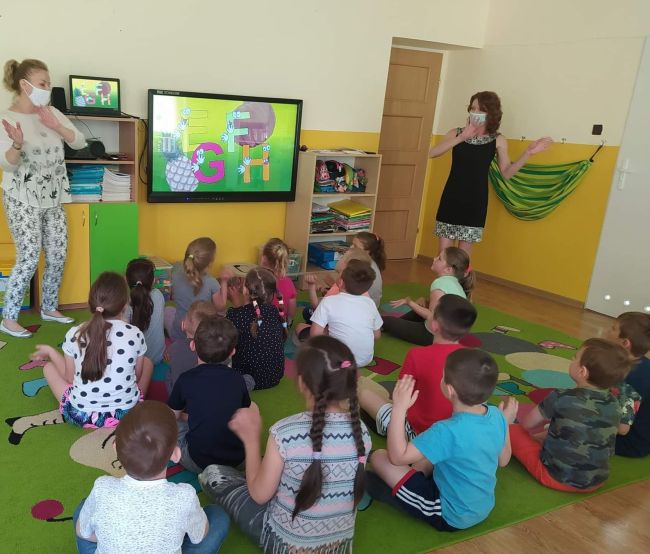 Przedszkolaki siedzą na dywanie, bawią się do piosenki 