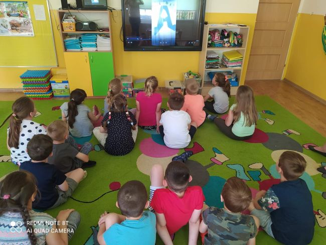 Przedszkolaki siedzą na dywanie i oglądają filmik przygotowany przez nauczycieli bibliotekarzy