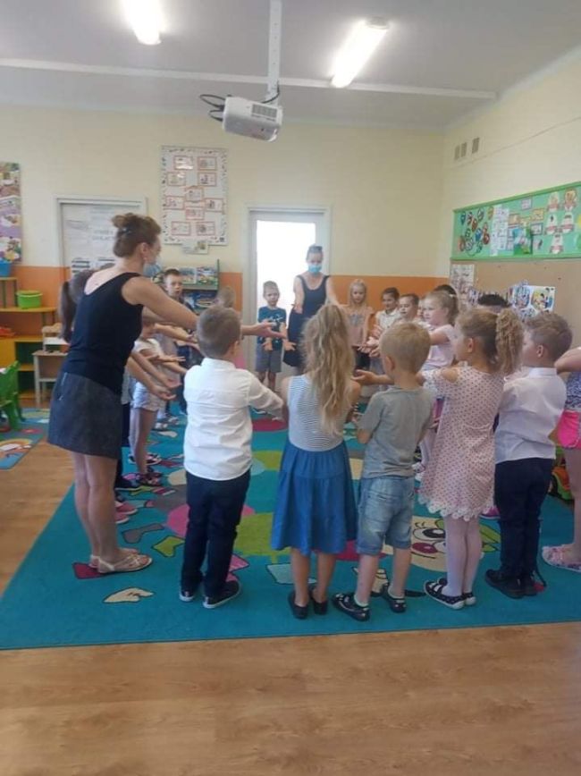 Dzieci wraz z nauczycielami bibliotekarzami stojące w kółeczku w sali przedszkolnej.