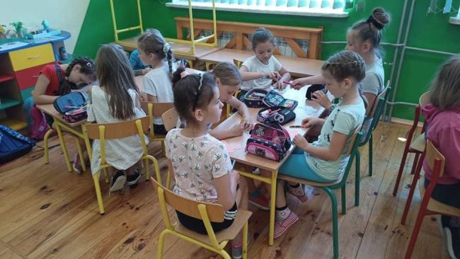 Dzieci siedzą przy stolikach i wykonują pracę plastyczną.