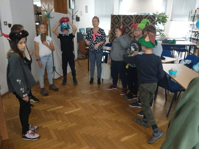 Przebrani czniowie siedzą w ławkach i słuchają nauczycieli prowadzących zajęcia. W tle tablica interaktywna z wizerunkiem Pana Kleksa z lektury 