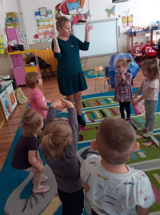 Nauczyciel prowadzi zabawę ruchową, dzieci naśladują jego gesty.