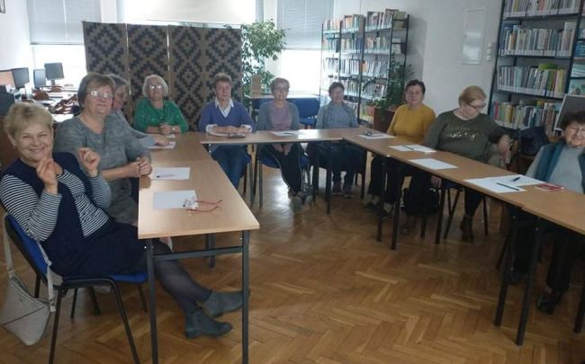 Słuchacze Uniwersytetu Trzeciego Wieku siedzą w ławkach.