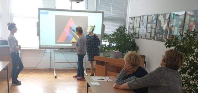 Prowadzące stoją przy tablicy. Uczestniczka warsztatów wykonuje zadanie wyświetlone na tablicy interaktywnej.