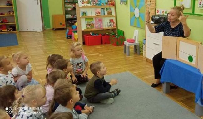 Sala przedszkolna. Dzieci siedzą na dywanie . Nauczyciel bibliotekarz prezentuje opowiadanie w teatrzyku Kamishibai.