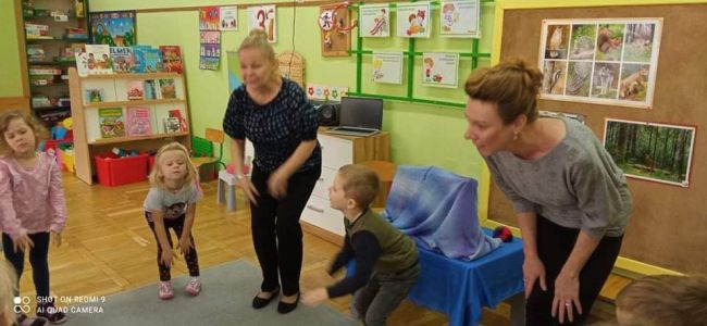Sala przedszkolna. Zabawa ruchowa. Dzieci wraz z prowadzącymi zajęcia ustawione w kręgu.