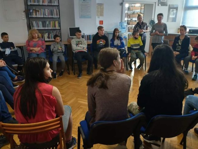 Uczniowie I opiekunowie siedzą w kręgu, na krzesłach. Nauczyciele bibliotekarze prowadza zajęcia.