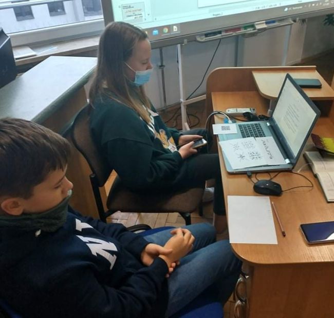Uczniowie siedzą przy biurku i laptopie, wykonują zadanie. 