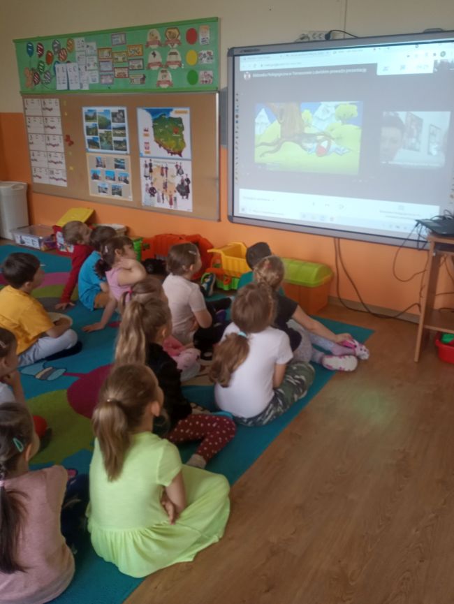 Przedszkolaki siedzą na dywanie przed ekranem. Oglądają prezentowany film “Polak mały”