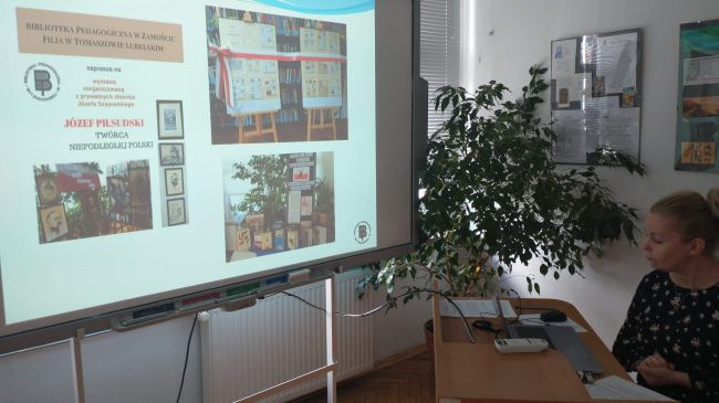 Nauczyciel bibliotekarz prowadzi zajęcia on-line. Prezentowane wystawy widoczne na tablicy interaktywnej