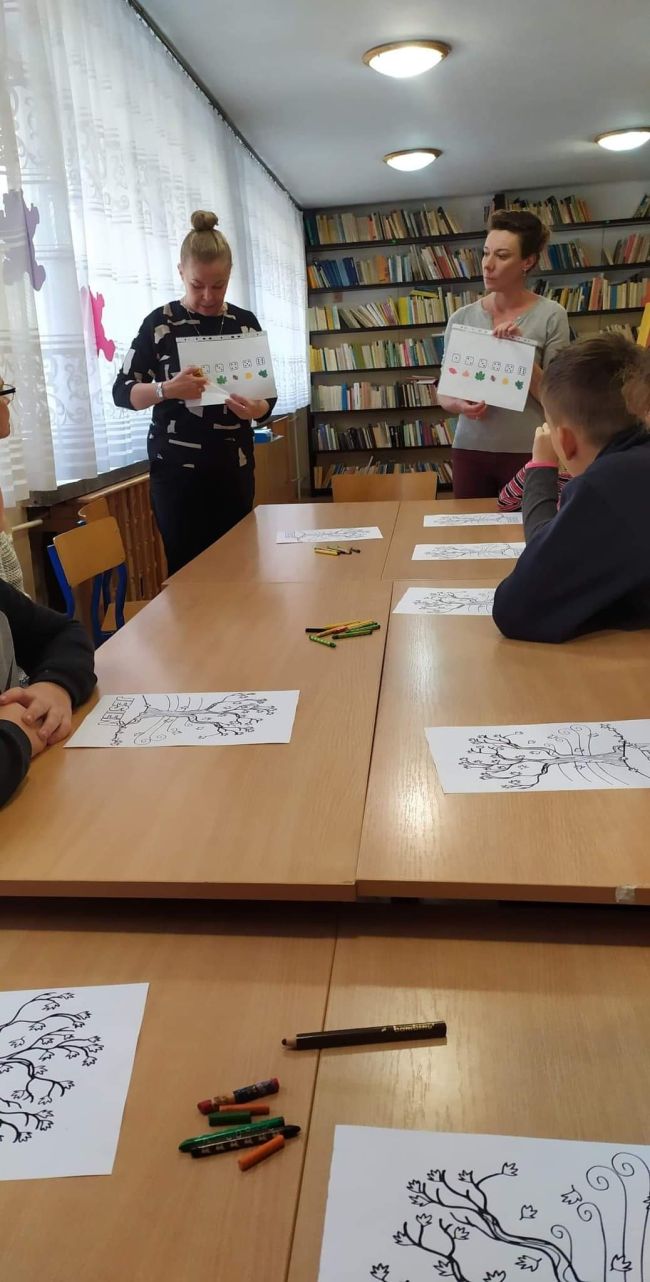 Nauczyciele bibliotekarze tłumaczą wykonanie zadania. W rękach trzymają plansze do gry planszowej.