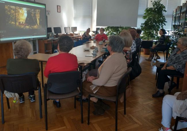 Prowadzące przedstawiają „Ballady i romanse” Adama Mickiewicza . Słuchacze Uniwersytetu Trzeciego Wieku w Tomaszowie Lubelskim oglądają na ekranie etiudę filmową „Świtezianka”
