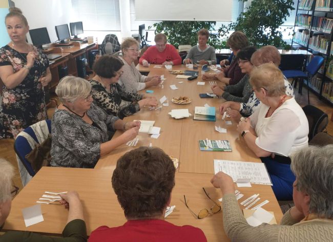 Seniorzy siedzą przy stołach. Wykonują ćwiczenie : układają wiersze  z rozsypanki 