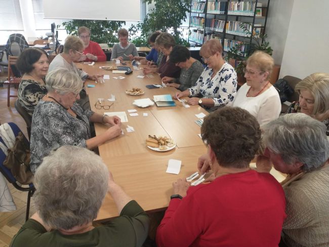 Seniorzy siedzą przy stołach. Wykonują ćwiczenie : układają wiersze  z rozsypanki 