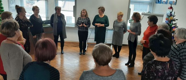 Seniorzy stoją w kręgu . Wykonują ćwiczenie na rozgrzewkę.
