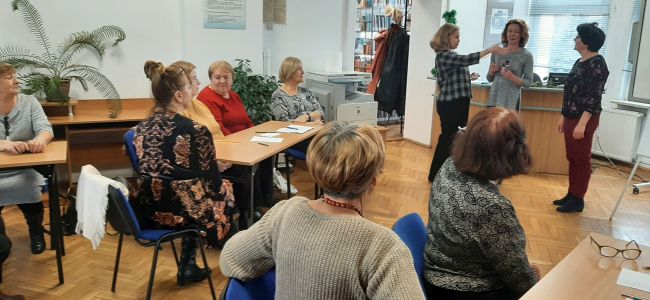 Seniorzy grają w Kalambury. Jedna osoba pokazuje hasło do odgadnięcia.