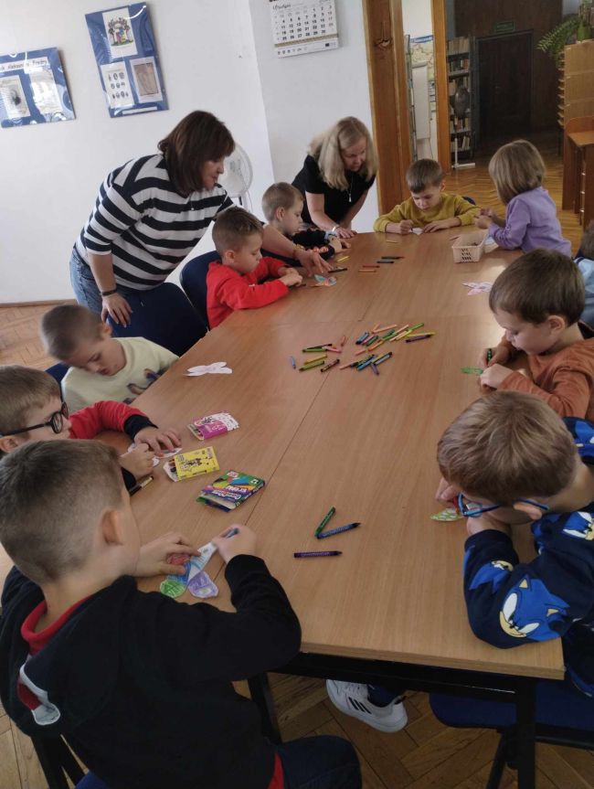 Praca plastyczna. Dzieci siedzą przy stole i kolorują motylki.