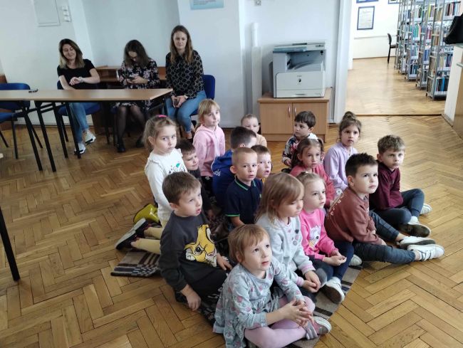 Przedszkolaki siedzą na podłodze, oglądają teatr Kamishibai