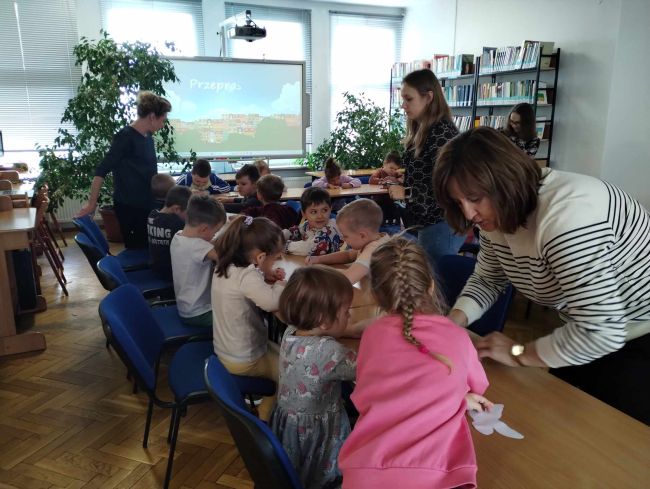 Praca plastyczna. Dzieci siedzą przy stole i kolorują motylki.