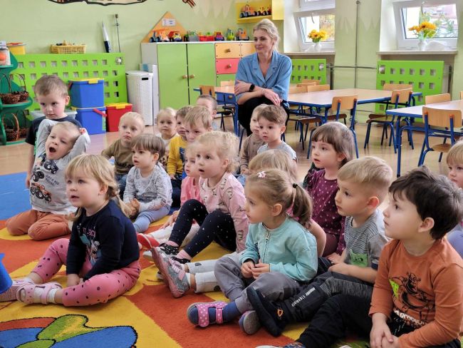 Dzieci siedzą na dywanie. Słuchają opowiadania o Myszce Pipi, prezentowanej za pomocą teatrzyku Kamishibai