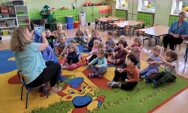 Dzieci siedzą na dywanie. Słuchają opowiadania o Myszce Pipi, prezentowanej za pomocą teatrzyku Kamishibai