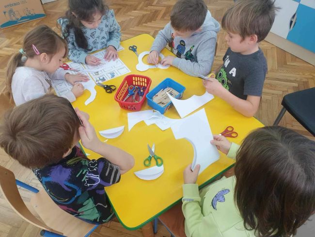 Dzieci przy stolikach wycinają misiowe buzie.