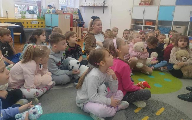 Dzieci z Pluszowym Misiem słuchają opowiadania o Misiu Tulisiu.