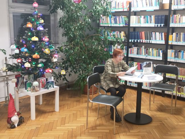 Poetka Agnieszka Kusmierczuk-Kubka siedzi przy stoliku i odczytuje swoje utwory.
