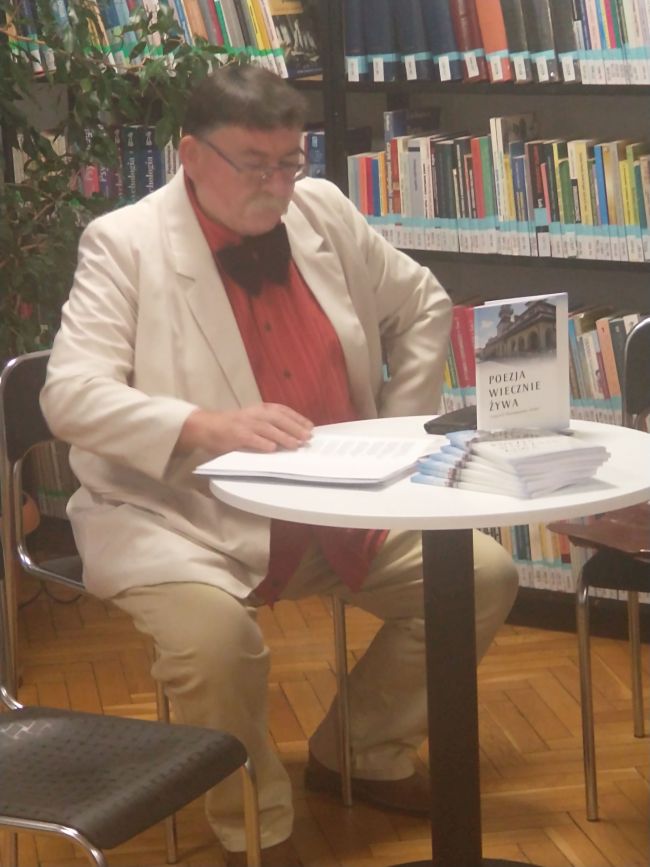 Poeta Jerzy Kij siedzi przy stoliku i prezentuje swoje utwory.