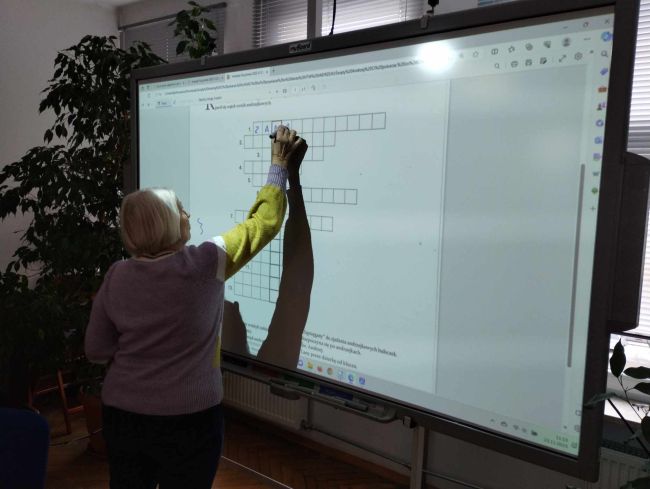 Na zdjęciu uczestniczka zajęć rozwiązuje krzyżówkę andrzejkową na tablicy interaktywnej