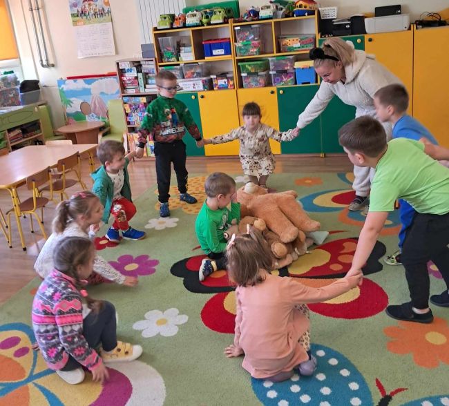 Dzieci siedzą na podłodze słuchają opowiadania o Misiu Tulisiu