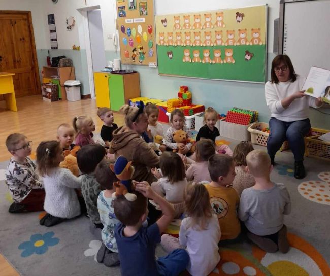 Dzieci siedzą na podłodze, rozmawiają z prowadzącą