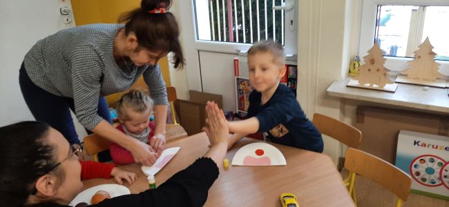 Dzieci siedzą przy stolikach i  wykonują pracę plastyczną